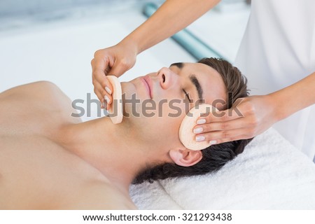 Close -up of a handsome young man receiving facial massage at spa center