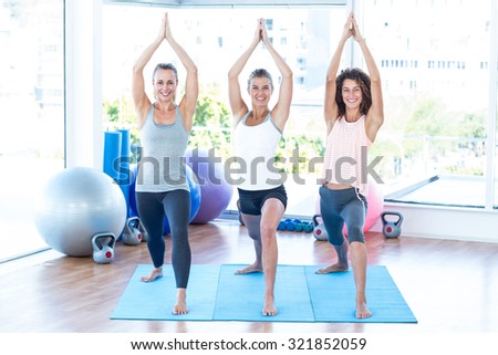 Happy women with joined hands in fitness studio while stretching on yoga mat
