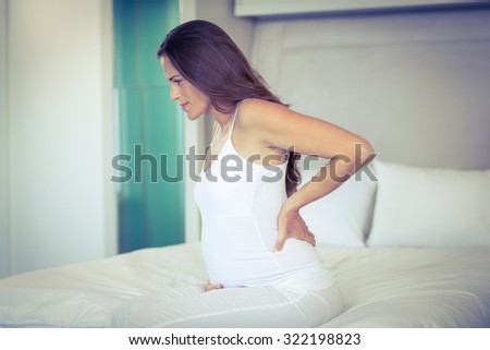 Pregnant woman sitting with back pain on bed