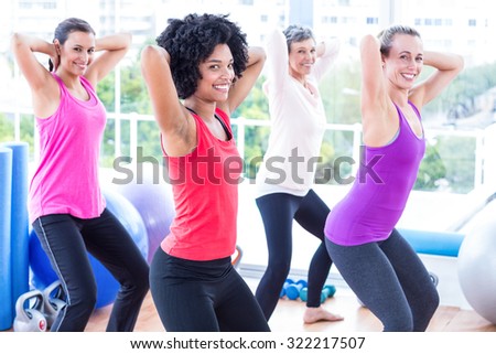 Portrait of smiling women exercising with hands behind head in fitness studio