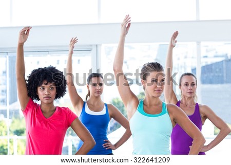 Focused woman in fitness studio with left arm raised while standing