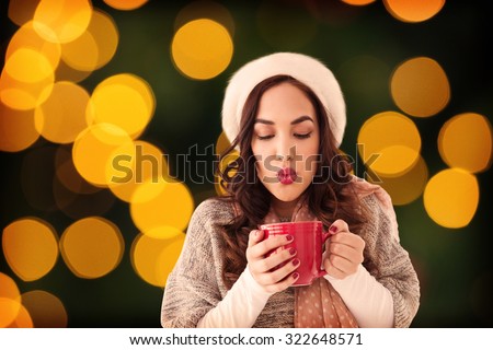 Brunette in winter clothes holding hot drink against blurry yellow christmas light circles