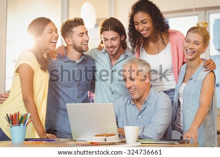 Happy business people looking at laptop in meeting room at creative office