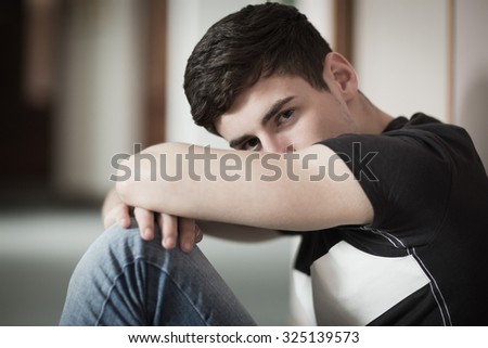Close-up portrait of male student with head on knees sitting by wall in college
