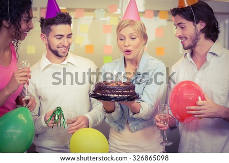 Businesswoman blowing birthday candles while colleagues looking at her in creative office
