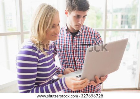 College friends working on laptop while standing by window