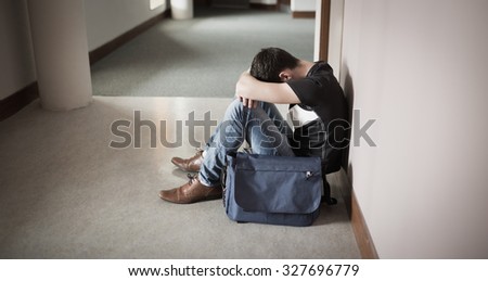 Depressed male student with head on knees sitting by wall in college