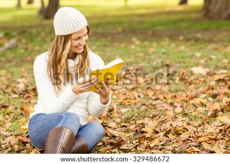 Smiling pretty woman reading a book in leaves on an autumns day
