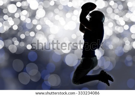 Silhouette American football player jumping while holding ball against glowing background