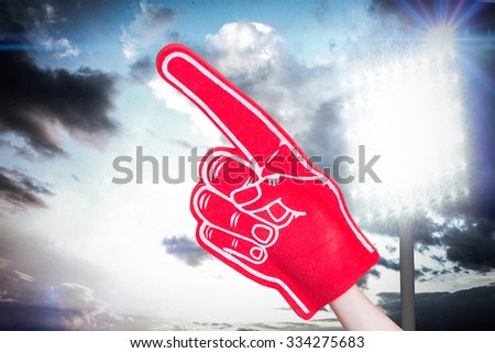 American football player holding supporter foam hand against spotlight in sky