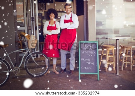 Snow against smiling colleagues in red apron with arms crossed