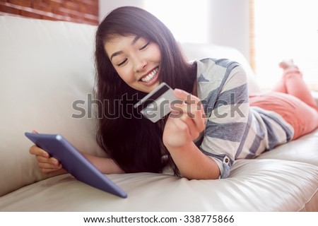Smiling asian woman on couch using tablet to shop online at home in the living room