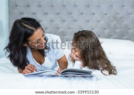 Happy mother and daughter reading a book on the bed at home