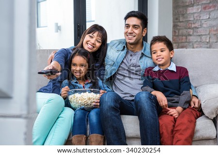 Happy young family eating popcorn while watching tv in living room