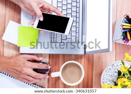 Overhead of feminine hands using smartphone and mouse with stuff on desk