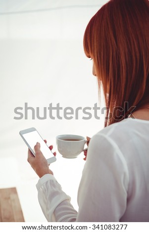 Back view of woman with red hair using smartphone and holding coffee cup