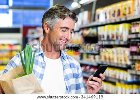 Smiling man with grocery bag using smartphone at the supermarket