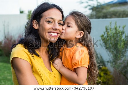 Cute daughter kissing her mothers cheek outdoors