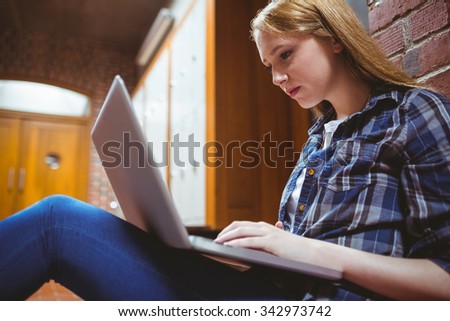Focused student sitting on the floor against the wall using laptop at the university