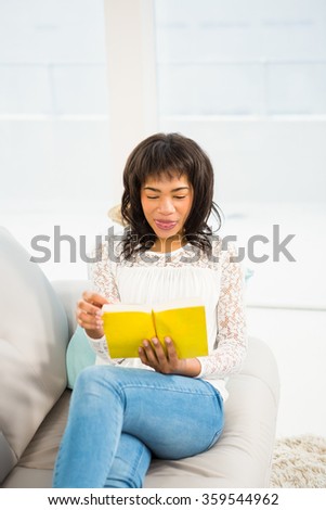 Casual smiling woman reading a yellow book at home