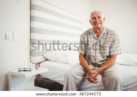 Portrait of senior man sitting on bed and smiling in bedroom