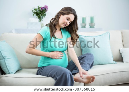 Pregnant woman massaging her tired feet on couch