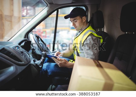 Delivery driver using tablet in van with parcels on seat outside warehouse