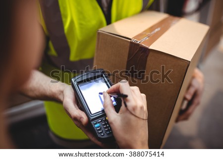 Woman signing on device to delivery parcel by van