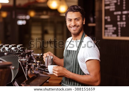 Handsome waiter adding milk to coffee at the cafe