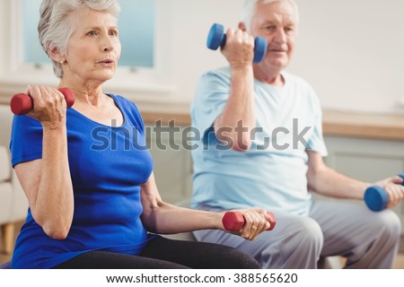 Senior couple lifting dumbbells while sitting on exercise ball at home
