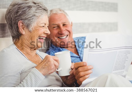 Senior couple laughing while reading newspaper in bedroom