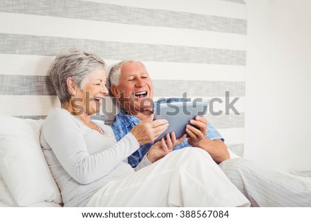 Senior couple laughing while using digital tablet in bedroom
