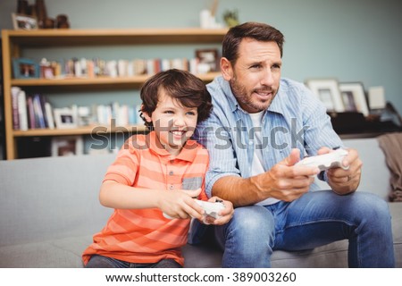 Father and son playing video game while sitting on sofa at home