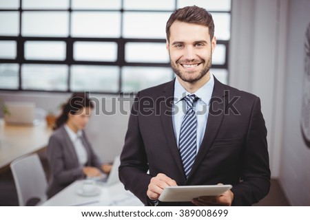 Portrait of confident young businessman using digital tablet while colleague in background