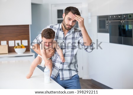 Portrait of frustrated father holding crying baby boy by table at home