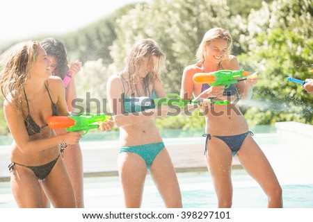 Happy friends doing water gun battle near swimming pool