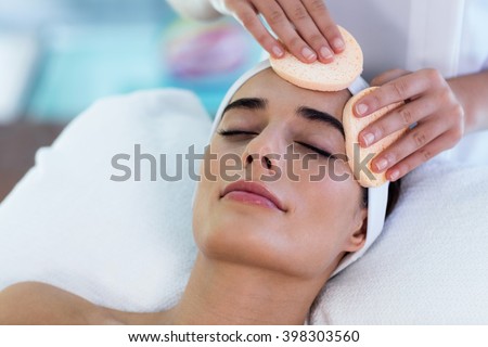 Masseuse cleaning woman face with cotton swabs at spa