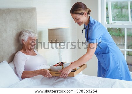 Happy nurse giving food to senior woman at home