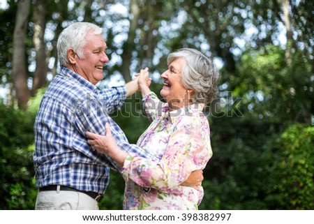 Cheerful senior couple dancing against trees in back yard