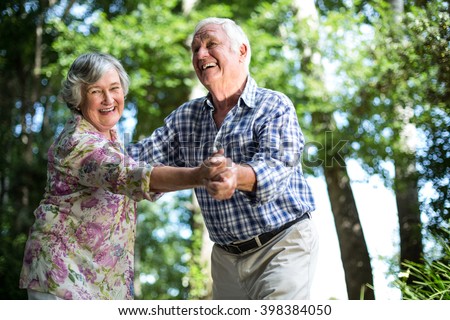 Happy senior woman dancing with husband against trees in back yard