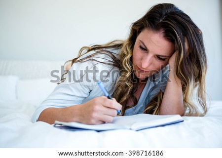 woman lying in her bed, looking sad and writing in a book