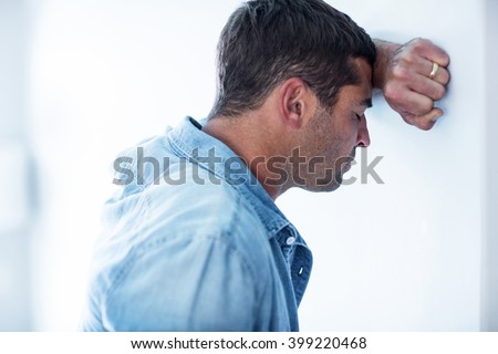 Close-up of upset man leaning on wall with hand on forehead