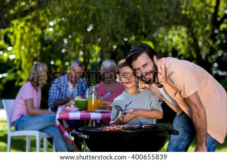 Smiling father with son by barbecue grill against family in yard