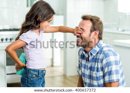 Girl hiding gift while covering happy father eyes in kitchen