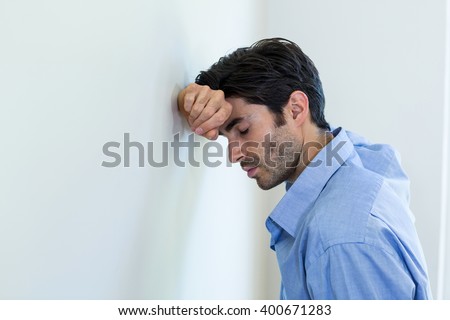 Depressed man leaning his head against a wall at home