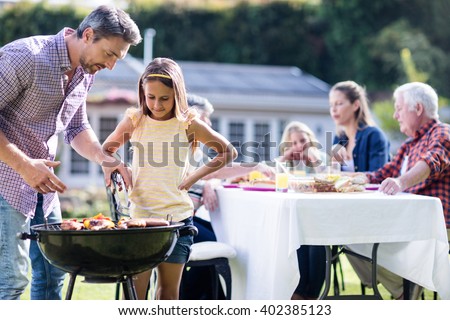 Father and daughter at barbecue grill while family having lunch in the garden