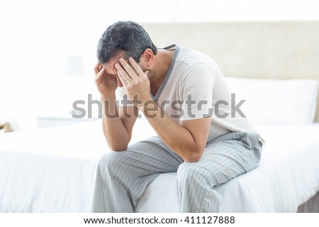Worried man sitting on bed with hand on forehead