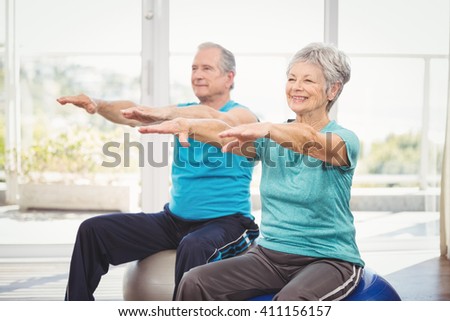 Happy senior couple performing exercise while sitting on exercise ball at home