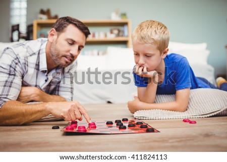 Close-up of father and son playing checker game while lying on floor at home