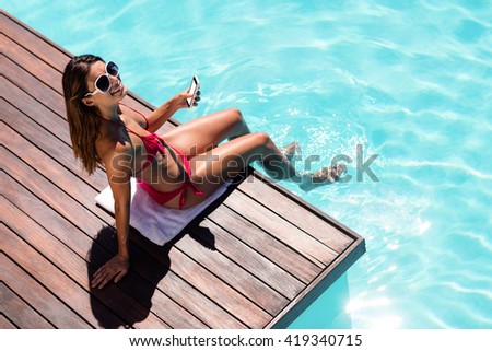 Woman using her smartphone on pool edge on a sunny day